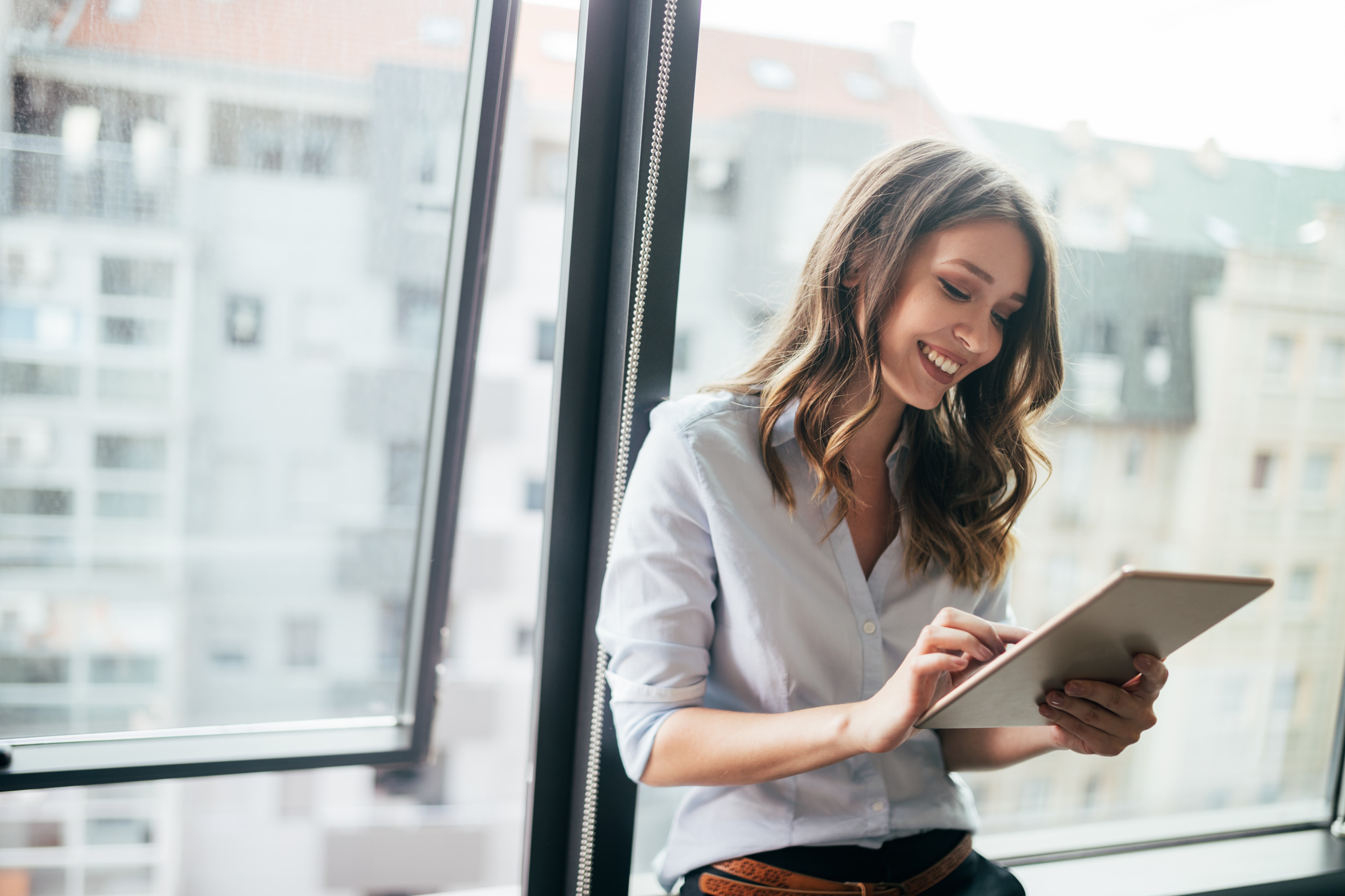 Businesswoman using a digital tablet while standing in front of windows.